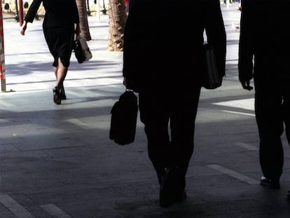 Un mujer y dos hombres de negocios pasean por una calle.