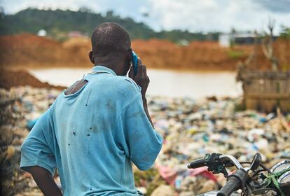 Hombre al teléfono frente a charca de 'galamsey' reconvertida en estercolero cerca de comunidad en Aowin.