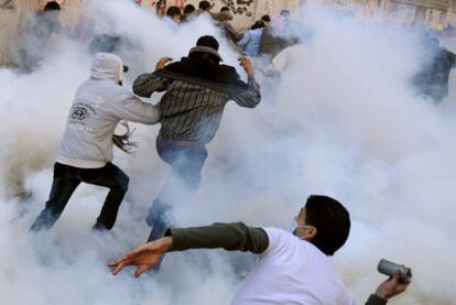 Un manifestante se dispone a devolver un bote de humo a las fuerzas de seguridad mientras otros huyen de la nube de gases lacrimógenos en la plaza de Tahrir.