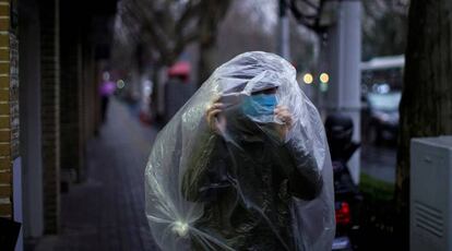 Un hombre con máscara y cubierto por plástico en Shanghái, China.