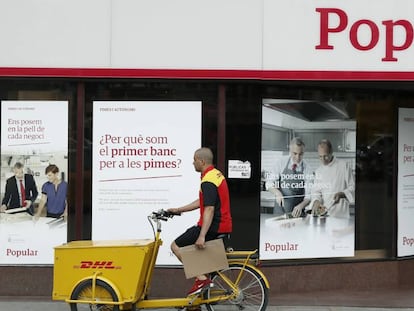 Un repartidor pasa por delante de una oficina del Banco Popular, en Barcelona.