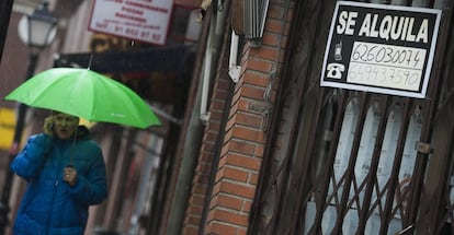 Una mujer camina por la calle frente a un cartel de alquiler de vivienda.