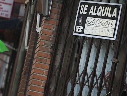 Una mujer camina por la calle frente a un cartel de alquiler de vivienda.