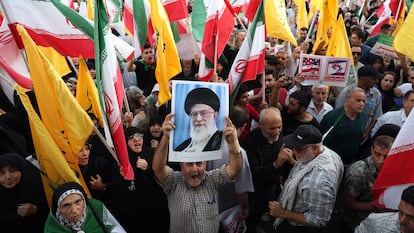Un iraní sostiene un retrato del líder supremo iraní, Alí Jameneí, entre banderas nacionales.