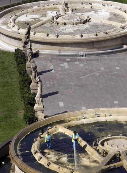 Dos operarios limpiando las fuentes vacías de la plaza de Catalunya de Barcelona, ayer.