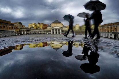 Varias personas se reflejan en un charco mientras se protegen de la lluvia con paraguas en el centro de Nápoles (Italia).