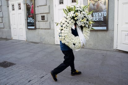 Un trabajador trae una corona de flores en la capilla ardiente.