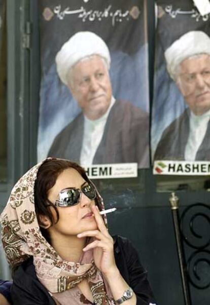 Una mujer fuma bajo carteles de campaña de Rafsanyani, en Teherán.