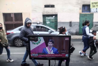 Durante sus primeros 12 meses de Gobierno, Castillo ha acumulado cinco investigaciones fiscales por presunta corrupción. Es el primer presidente peruano investigado en funciones. En la imagen, personas pasan delante a un televisor mientras Castillo ofrece su mensaje al Congreso durante la conmemoración del 201 aniversario de la independencia peruana, en Lima, el 27 de julio de 2022.