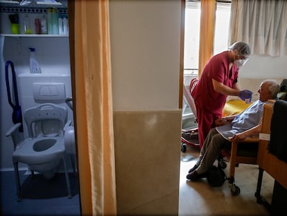 Un empleado cuida de un hombre mayor en una de las habitaciones en la residencia de ancianos Santa María de Montecarmelo, en Madrid.