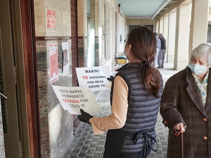 Una camarera coloca carteles de reducción de aforo y barra cerrada por la covid-19, en Pamplona.