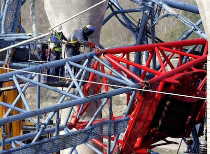 Unos operarios de la constructora responsable de la obra seccionan la grúa accidentada para facilitar su desmontaje. Se desconoce cuánto durarán los trabajos para abrir la vía.