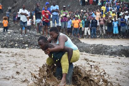 TOPSHOT - A man carries a woman across a  river at Petit Goave where a bridge collapsed during the rains of the Hurricane Matthew, southwest of Port-au-Prince, October 5, 2016. 
Haiti and the eastern tip of Cuba -- blasted by Matthew on October 4, 2016 -- began the messy and probably grim task of assessing the storm's toll. Matthew hit them as a Category Four hurricane but has since been downgraded to three, on a scale of five, by the US National Hurricane Center. / AFP PHOTO / HECTOR RETAMAL