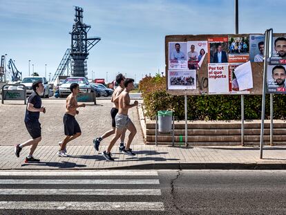 Un grupo de corredores pasan por delante de una valla publicitaria llena de carteles electorales en Sagunto.