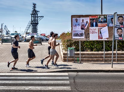 Un grupo de corredores pasan por delante de una valla publicitaria llena de carteles electorales en Sagunto.