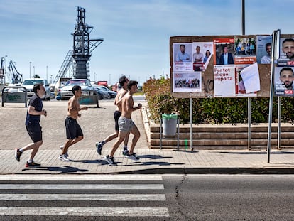 Un grupo de corredores pasan por delante de una valla publicitaria llena de carteles electorales en Sagunto.