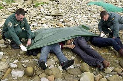 Dos guardias civiles cubren los cuerpos de tres inmigrantes ahogados en la costa de Tarifa.