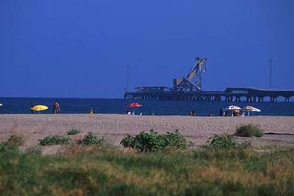 La playa del puerto de Sagunto, en la comarca valenciana de El Camp de Montvedre. Al fondo, pasarela industrial para el transporte de mercancías.