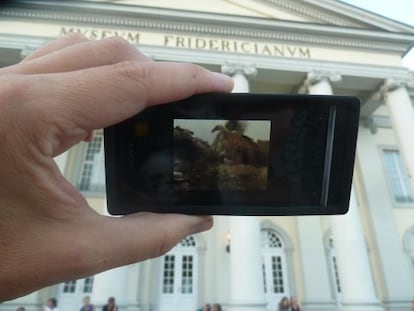 El artista muestra la aplicación que aparece en los móviles, frente al museo de Kassel, sede de la Documenta.