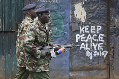 Dos oficiales pasan junto a un mensaje de paz escrito en la pared mientras intentan dipersar a los partidarios del candidato opositor Raila Odinga, en Kiberia, el mayor barrio chabolista de Nairobi (Kenia) el 10 de agosto.