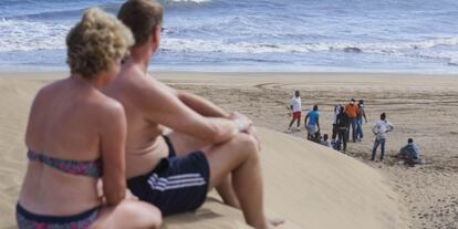 Dos turistas observan al grupo de inmigrantes aislados el mi&eacute;rcoles en la playa de Maspalomas.