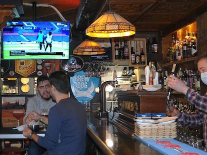 Víctor Rey sirve unas cervezas en su bar, El rincón del Greco. De fondo, un informativo de LaLiga Santander. 