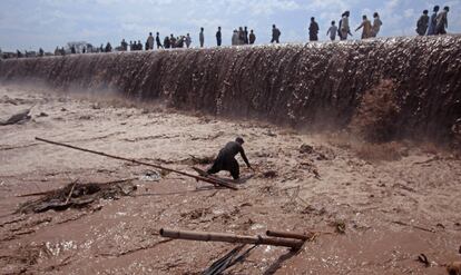 Un comerciante trata de salvar sus pertenencias mientras los residentes usan un puente inundado tras una fuerte lluvia a las afueras de Peshawar (Pakistán), el 4 de abril de 2016.