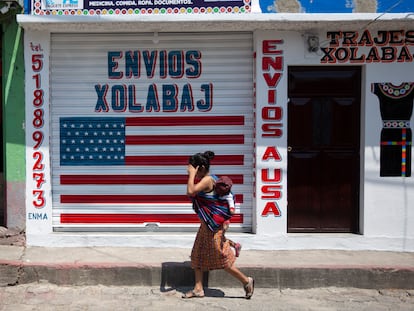 Una mujer pasa con su hijo frente a un local de envíos hacia y desde EE UU en Joyabaj (Guatemala).