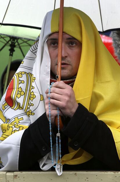Un hombre, ataviado con una bandera del vaticano reza mientras espera la fumata en el segundo día de la votación para elegir nuevo papa.
