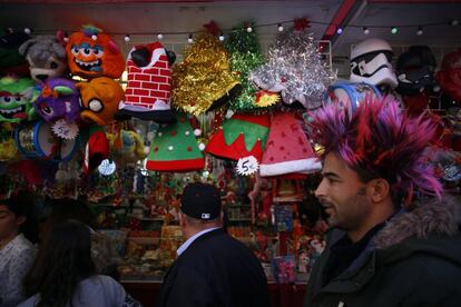 Un hombre ataviado con una colorida peluca pasa por un puesto de venta de complementos navideños en el centro de la capital.