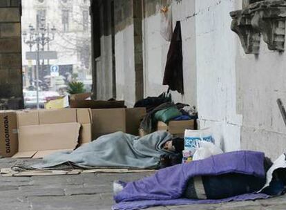 Varias personas sin hogar protegiéndose del frío con cartones y mantas en pleno centro de Bilbao.