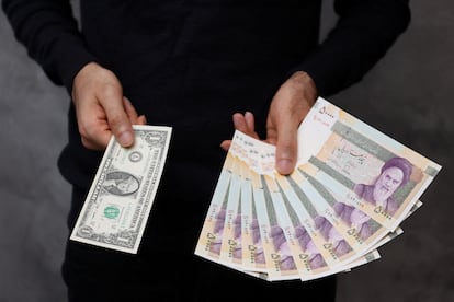 A currency dealer poses for a photo with a U.S one dollar bill and the amount being given when converting it into Iranian rials in an exchange shop in Tehran, Iran December 25, 2022.