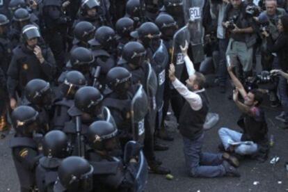 Dos manifestantes con los brazos levantados frente a dos filas de agentes antidisturbios en el 25-S.