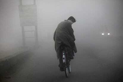 El ciclista, en medio de una espesa niebla, mira a cámara mientras no detiene su avance por una de las calles Srinagar.