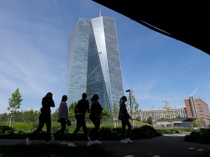 Cinco personas pasean por un parque con la sede del Banco Central Europeo al fondo, en Fráncfort.