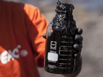 Un miembro de Greenpeace ense&ntilde;a un bote con muestras del combustible que ha llegado en las &uacute;ltimas horas a la playa de Venegueras, en el municipio grancanario de Mog&aacute;n.