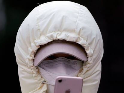 Una mujer con una máscara revisa su teléfono móvil.