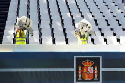 Dos operarios trasladan sillas en una de las tribunas instaladas en la plaza de Neptuno de Madrid para seguir el desfile de hoy.