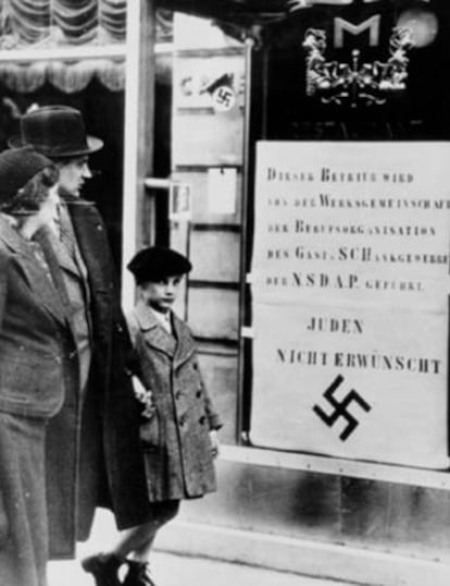 Una familia judía pasa ante un escaparate con un cartel contra los judíos, en una calle de Viena, en 1938.