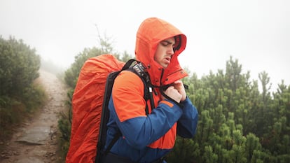 Un hombre caminando por el campo con una funda puesta en su mochila.