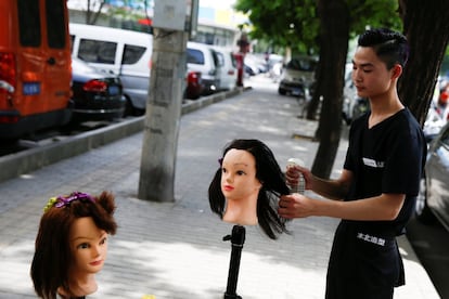 Un aprendiz de peluquería practica con dos maniquíes en el exterior de un salón de belleza de Pekín (China).