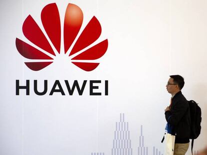 Un hombre pasa junto a un logo de Huawei, mientras otro habla por móvil en una exposición en Pekín.