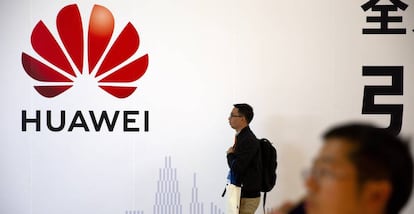 Un hombre pasa junto a un logo de Huawei, mientras otro habla por móvil en una exposición en Pekín.