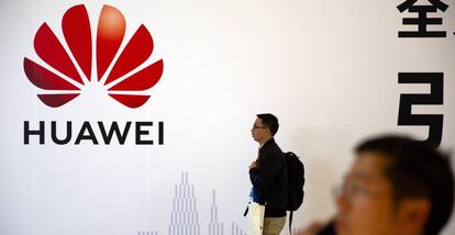 Un hombre pasa junto a un logo de Huawei, mientras otro habla por móvil en una exposición en Pekín.