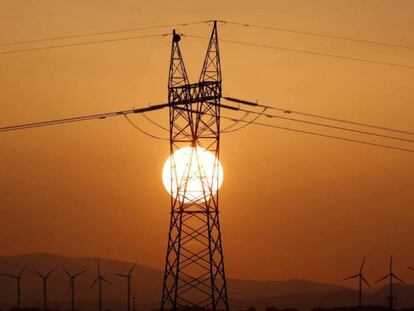 Torre del tendido eléctrico, en primer término, y molinos de viento al fondo.