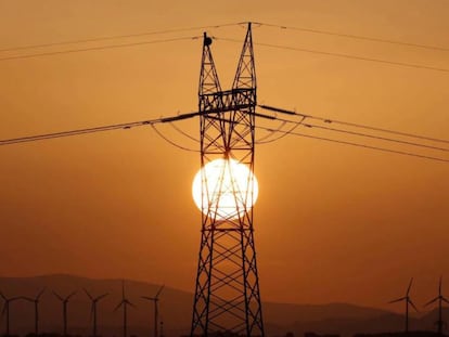 Torre del tendido eléctrico, en primer término, y molinos de viento al fondo.