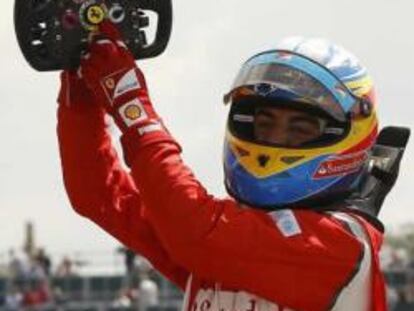 El piloto español de Fórmula 1, Fernando Alonso, señala el emblema de la escudería Ferrari en el volante de su vehículo, tras vencer en la carrera del GP de Gran Bretaña.