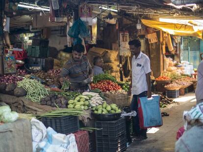 Un hombre con una bolsa de tela para hacer la compra adquiere legumbres en un mercado de Bombay.
