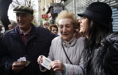 Una persona de avanza edad porta el segundo premio de la Lotería del Niño, el 69362, vendido en la la administración de la calle Marqués de Corbera en La Elipa, Madrid.