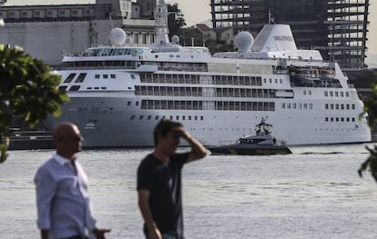 Duas pessoas caminham, tendo o barco Silver Cloud, o cruzeiro dos EUA, ao fundo.